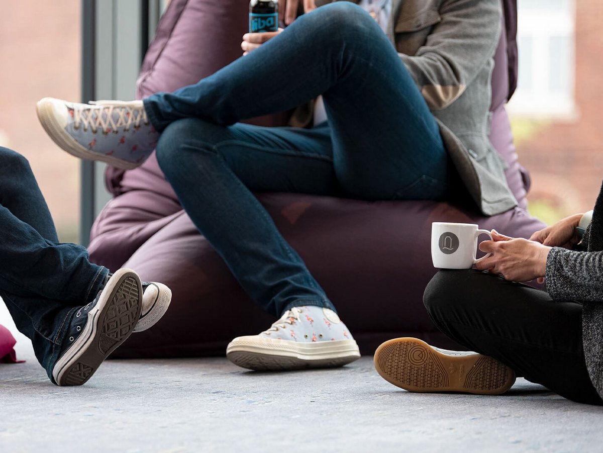 Drei Personen sitzen in Sitzsäcken und auf dem Boden und trinken Kaffee
