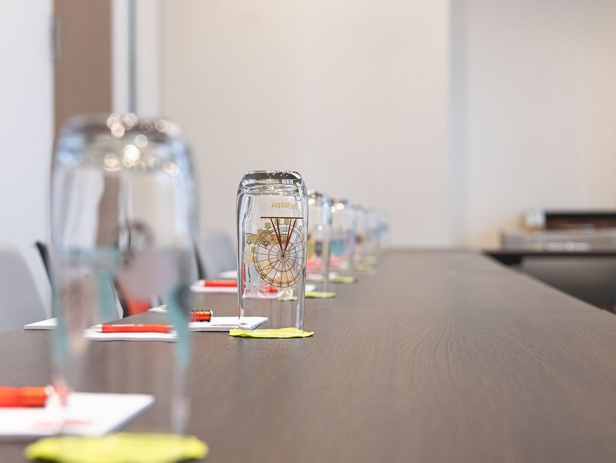 Eingedeckter Tagungstisch mit Wasserglas, Blöcken und Stiften 