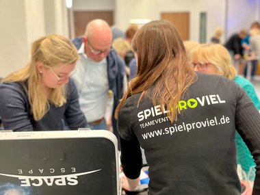 Menschen die um eine Metallbox stehen und rätseln