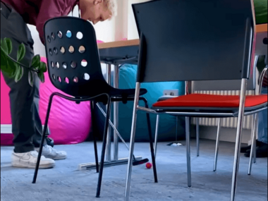 Ein Mann spielt zwischen einem Tagungstisch und Stühlen Minigolf