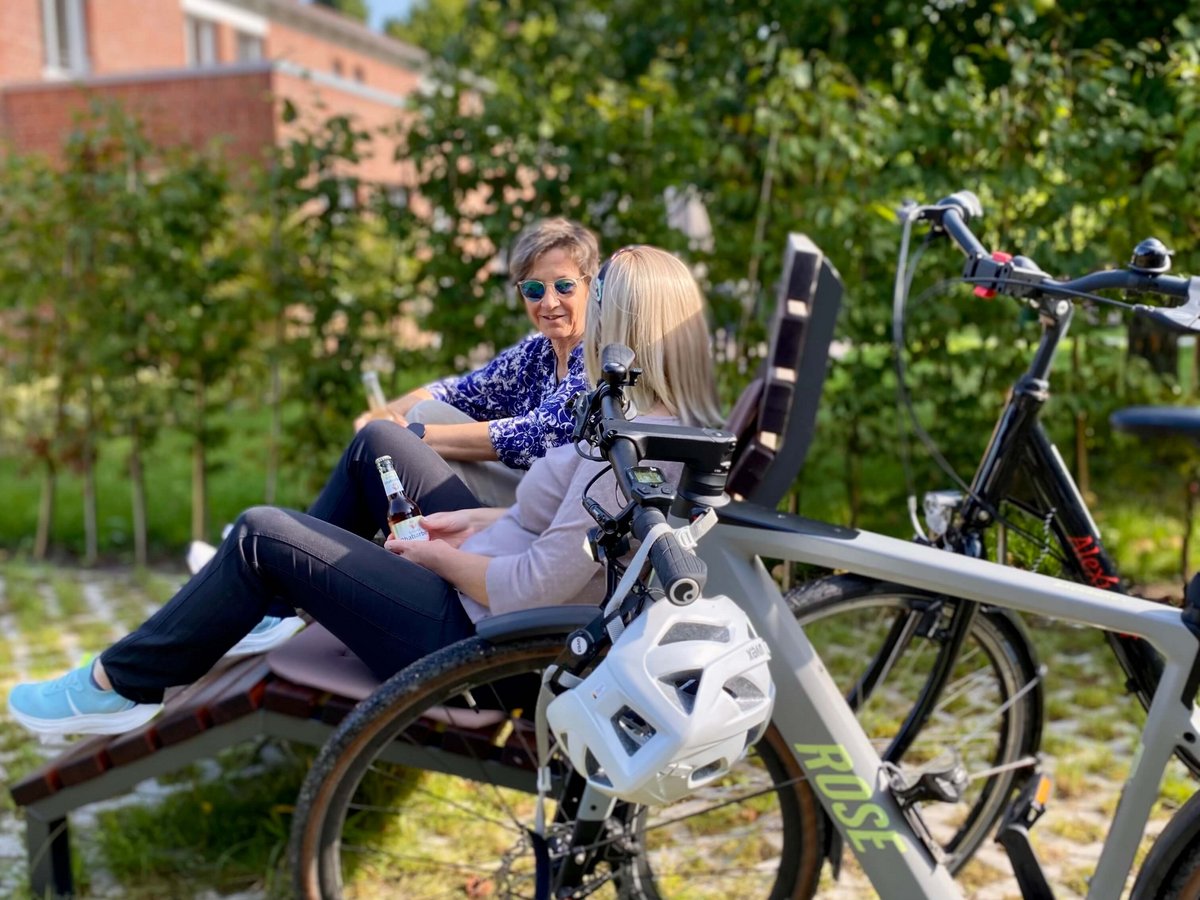 Zwei Frauen, die auf einer Bank sitzen. Davor stehen Fahrräder. 