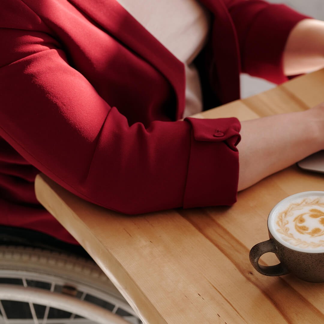 Ein Mensch mit Rollstuhl sitzt am Laptop mit Kaffee und Frühstück 