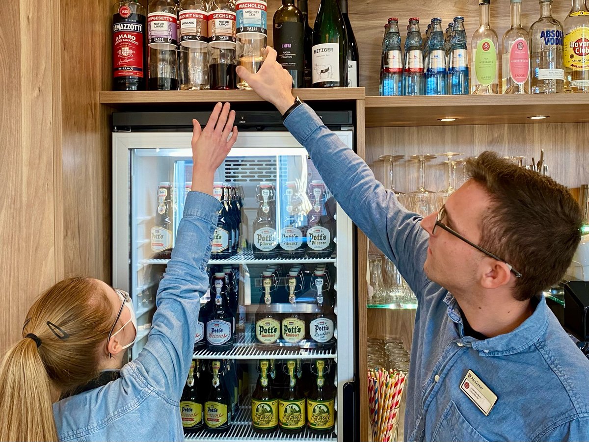 Eine Mann hilft dabei ein Flasche aus einem hohem Regal herunter zu nehmen. 