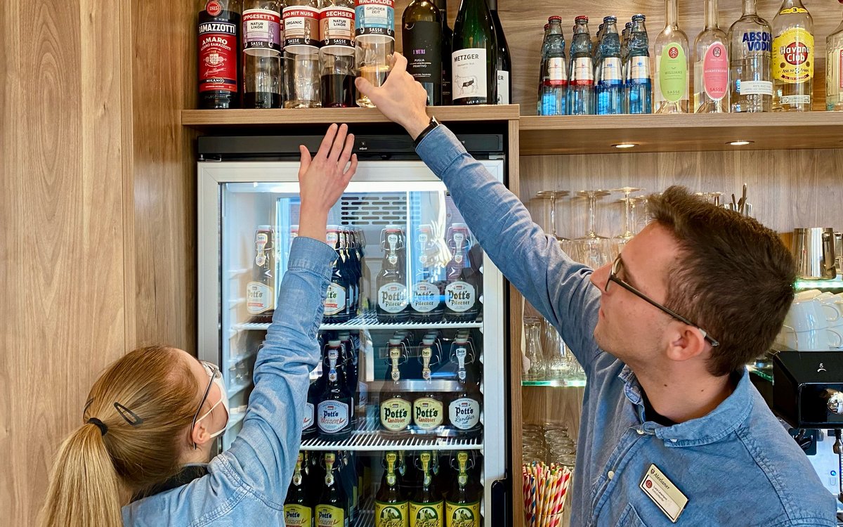 Eine Mann hilft dabei ein Flasche aus einem hohem Regal herunter zu nehmen. 
