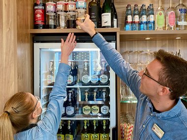Eine Mann hilft dabei ein Flasche aus einem hohem Regal herunter zu nehmen. 