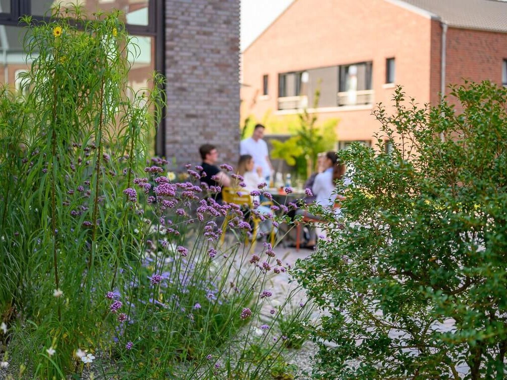 Eine Gruppe von Gästen sitzt vom Gebäude zwischen grünen Pflanzen