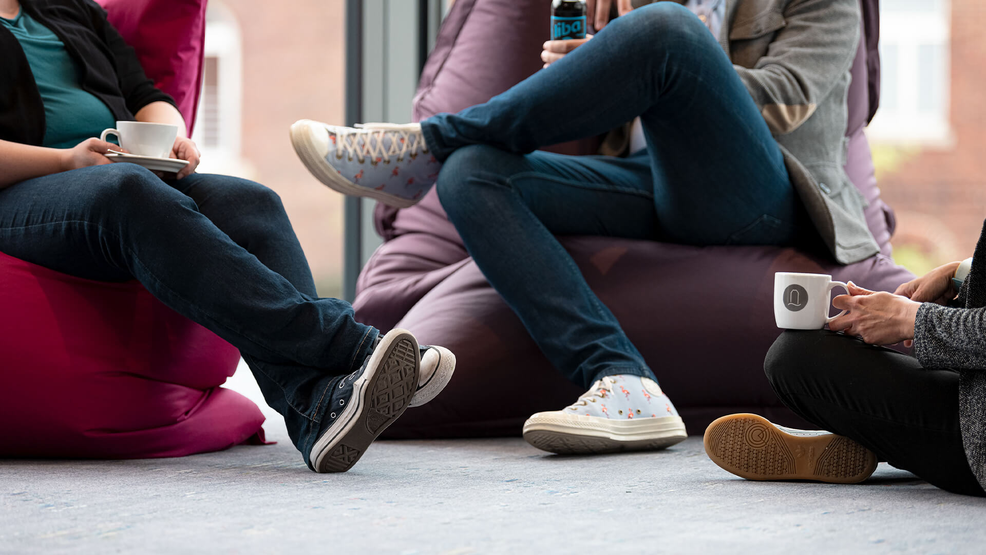 Drei Personen sitzen in Sitzsäcken und auf dem Boden und trinken Kaffee